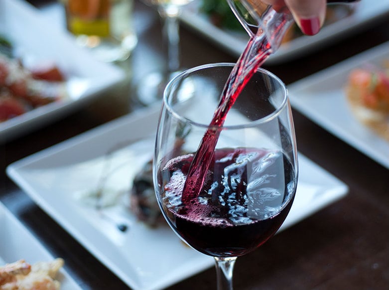 a glass of red wine being poured in front of several plates of tapas