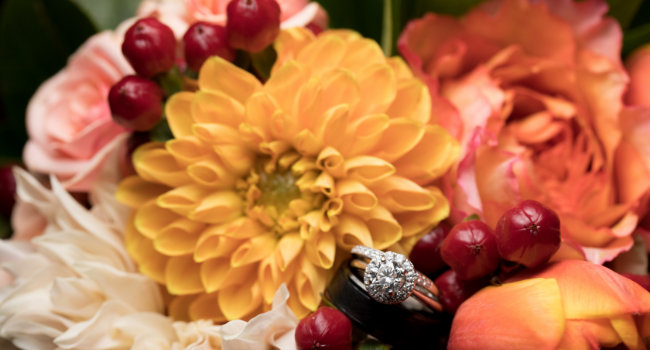 A decorative picture of yellow, peach and red flowers with a diamond wedding ring.