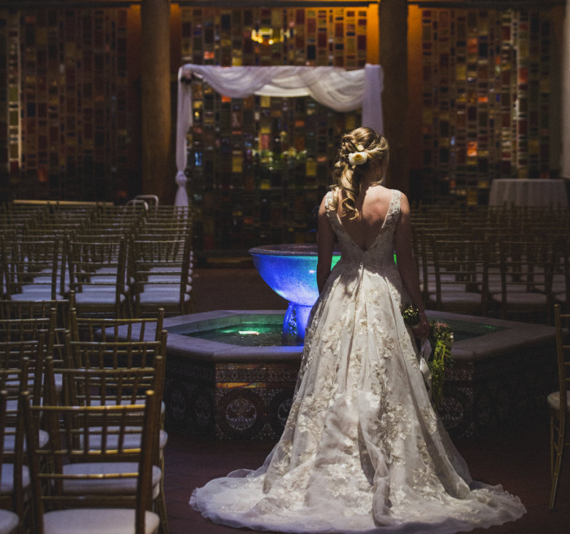 A bride poses facing away from the camera showing off a beautiful white dress in near the lobby fountain at Hotel Andaluz.